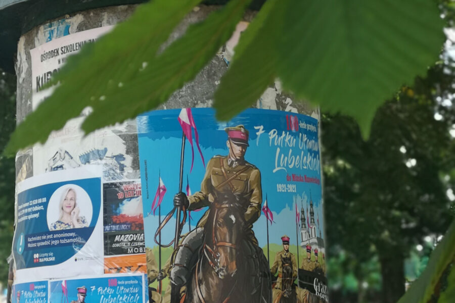 Słup ogłoszeniowy z plaktem reklamującym obchody 100-lecie przybycia 7 Pułku Ułanów Lubelskich do Mińska Mazowieckiego. W górnej części fotografi liść kasztanowca.